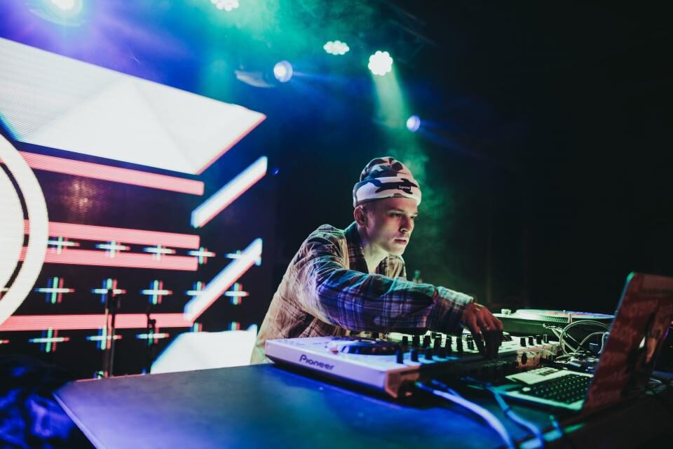 A DJ performing behind decks under stage lighting