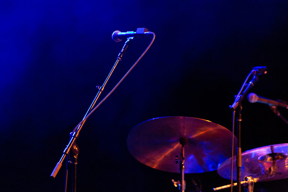 A microphone and drum kit lit in blue on a small live stage