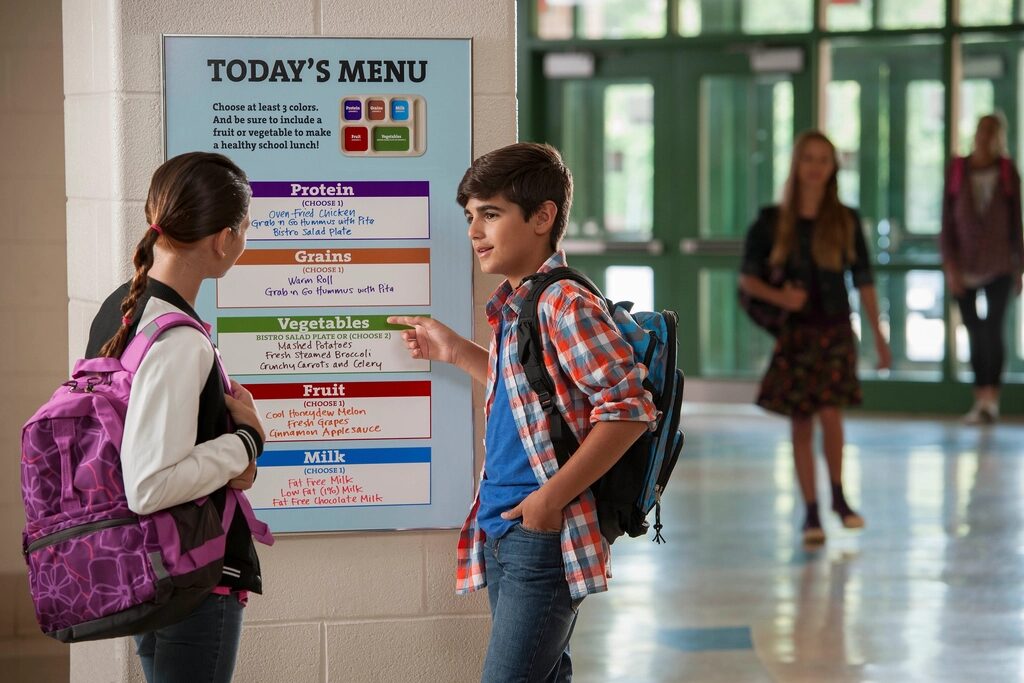 Two students reading a menu board in a school hallway